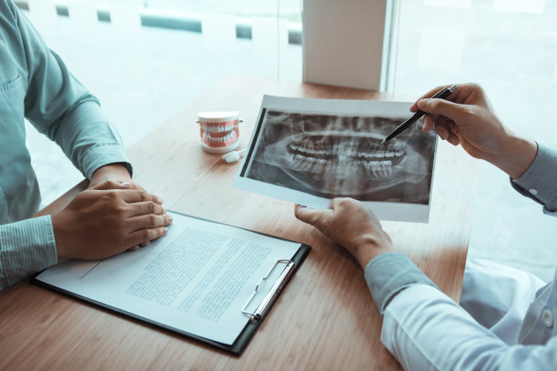 牙医手持笔指点x光照片，并与患者谈论药物和手术治疗。图片下载