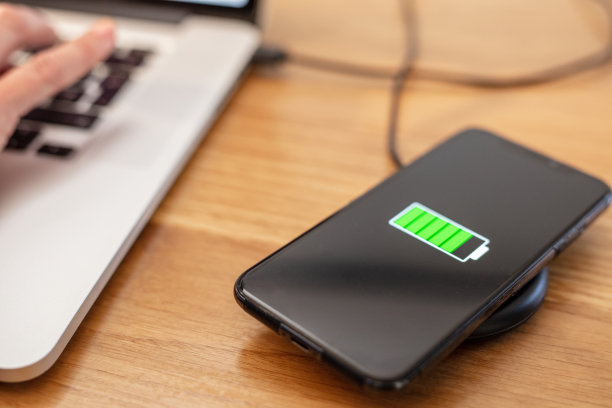 靠近智能手机充电的无线充电器上的笔记本电脑图片下载