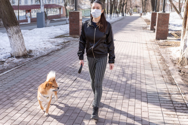 疫情期间，戴口罩的女人在房子附近遛狗素材图片