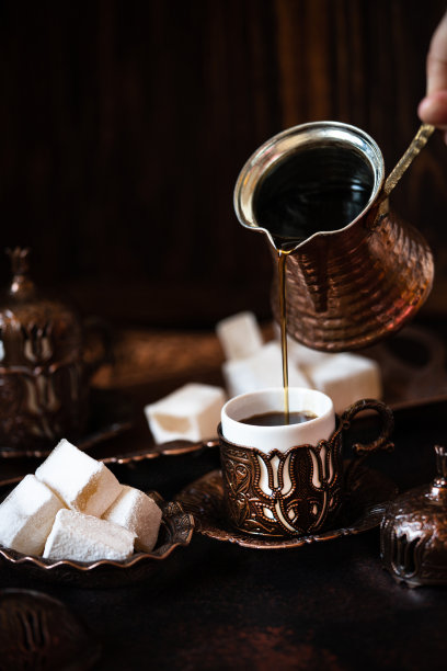 传统的土耳其咖啡和土耳其软糖在传统的东方铜餐具。咖啡从cezve倒进杯子。暗的背景图片下载