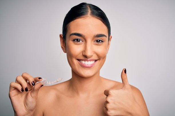年轻美丽的黑发女人拿着牙齿矫正器矫正牙齿，开心地笑着做ok的手势，大拇指向上的手指，优秀的手势图片下载