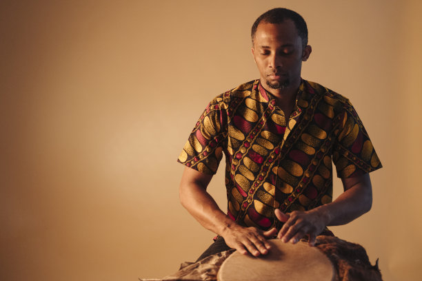 在棕色背景下演奏传统鼓的非洲裔男音乐家图片下载