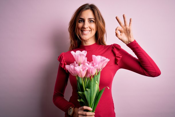年轻漂亮的黑发女子拿着粉色郁金香花束，面带微笑，用手和手指做出OK手势，表达成功图片下载