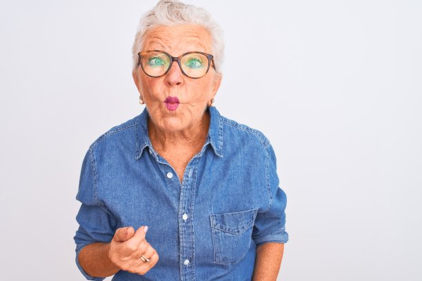 穿着牛仔衬衫、戴眼镜的年长白人妇女在白色背景前做鬼脸图片下载