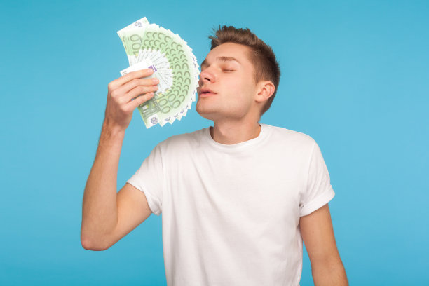 贪婪和金钱。年轻的商人穿着休闲的白色t恤，闻着欧元钞票，神情愉悦图片下载