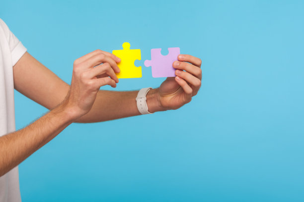 特写的男性手拿着两个拼图部分，准备连接彩色拼图块，象征团结和联系图片下载