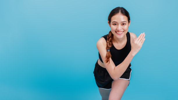 自信美丽的亚洲健身女性在蓝色背景上热身运动的肖像图片下载
