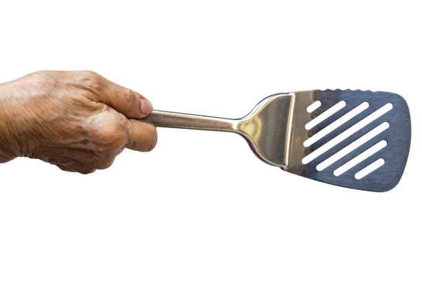 妇女的右手拿着不锈钢锅铲烹饪在白色的背景，近距离拍摄，选择性聚焦，厨房用具的概念图片下载