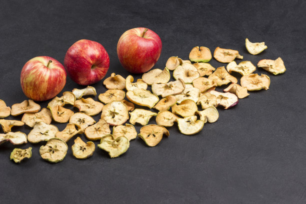 三个新鲜的红苹果和几片干苹果在黑色的背景下。素食点心图片下载