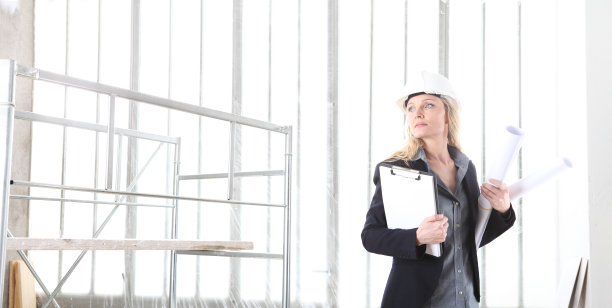 建筑工地内的女工程师，手持文件夹和蓝图图片下载