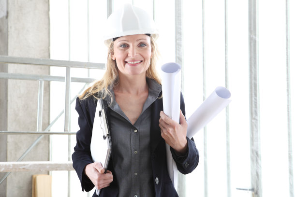 建筑工地内戴头盔、拿文件夹和蓝图的微笑女建筑师或工程师图片下载