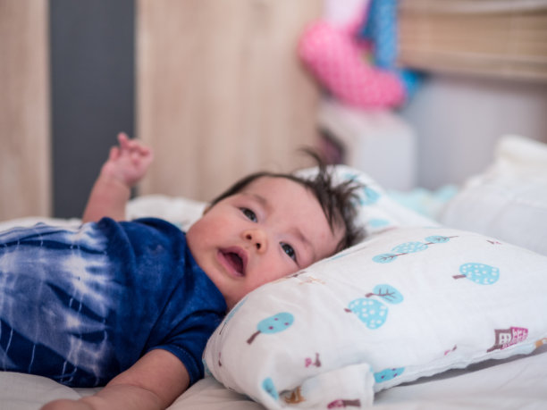 可爱的宝宝穿着蓝色婴儿服躺在床上，举起右臂图片下载