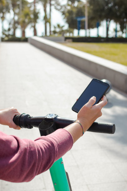 在大街上骑着电动车并使用手机的人。用智能手机的应用程序租一辆滑板车，复制空间顶部。图片下载