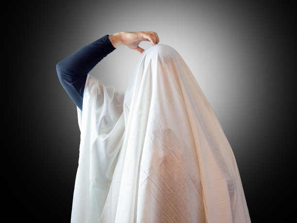 一个像鬼一样盖着白床单的男人，用手在有背光的黑暗背景上抓着自己的头图片下载