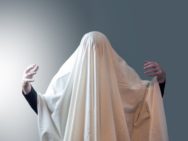 那个人，像幽灵一样裹着白色的衣服，在灰色的背景下把手从衣服下面抽出来，左边有灯光图片下载