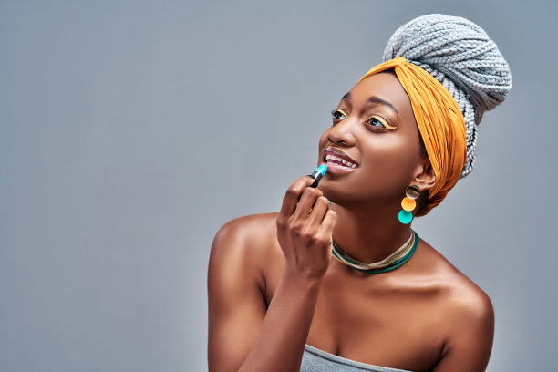 漂亮的女孩正在涂口红。照片的非洲裔美国女孩的侧面在灰色的背景。护肤美容图片下载