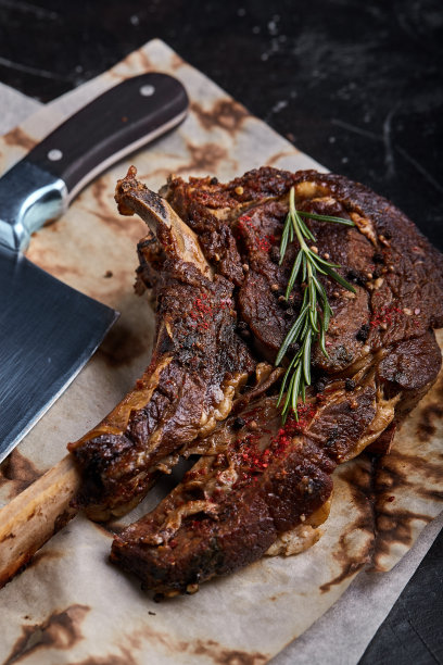 战斧牛排，蔬菜和刀放在桌上。桌上有烤肉、烤蔬菜和新鲜蔬菜图片下载