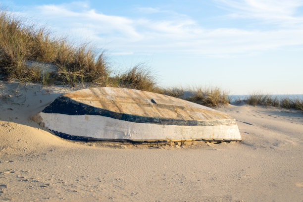 蓝白相间的木船被遗弃在沙滩上，背景是大海，天空是白云。图片下载