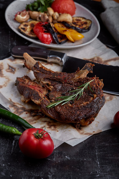 战斧牛排，蔬菜和刀放在桌上。桌上有烤肉、烤蔬菜和新鲜蔬菜图片下载