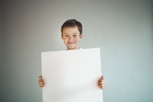 男孩在灰色背景前举着白色的牌子图片下载