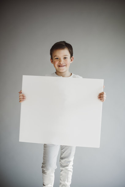 男孩在灰色背景前举着白色的牌子图片下载