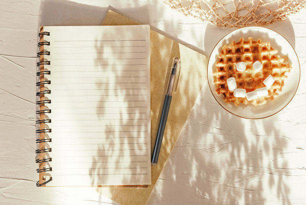 棉花糖华夫饼微笑和笔记本在白色纹理的桌子上。平面构成。图片下载