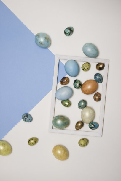 彩色的复活节彩蛋在一个木制的白色框架，并在它旁边的白色和蓝色的背景。文本的空闲空间。图片下载