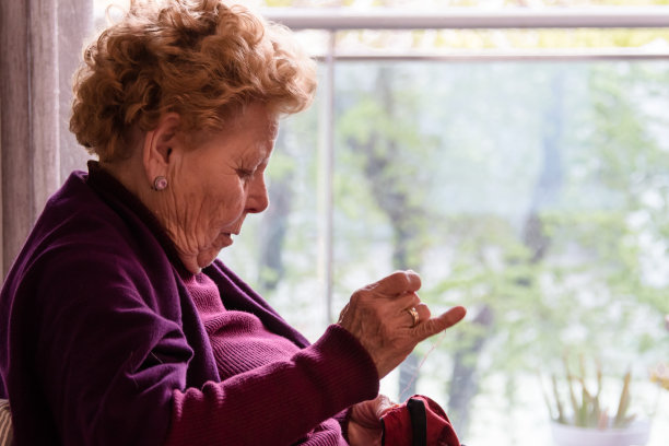 老年妇女坐在窗边缝纫图片下载