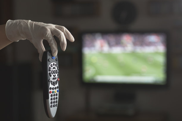 手持电视遥控器与医疗手套。待在家里和新冠肺炎概念。图片下载