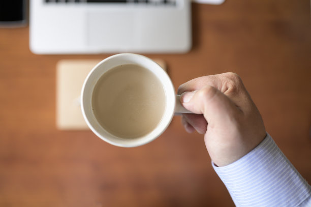商人的手拿着一杯咖啡在办公桌上图片下载