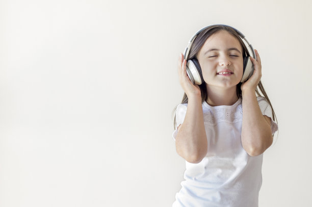 一个穿着白色衬衫的黑发小女孩的肖像，戴着大大的无线耳机，听着音乐，闭着眼睛唱歌跳舞，没有人在家素材图片