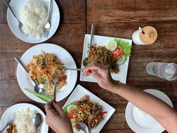 俯视图妇女手握勺子与炒面和米饭在木桌上。图片下载