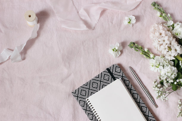 春天，婚礼文具模型现场。花束的婴儿呼吸吉普赛花，风信子和马提奥拉花在粉红色的亚麻背景。空白笔记本，银色钢笔。平躺，俯视图。图片下载