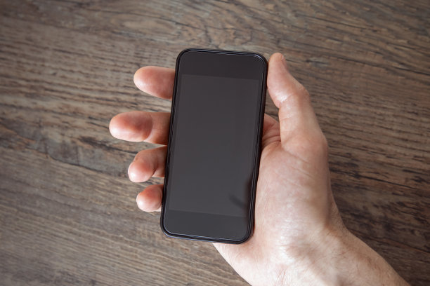 男子左手拿着空白手机，空白显示近距离，中性背景，从上面看。等待电话。图片下载