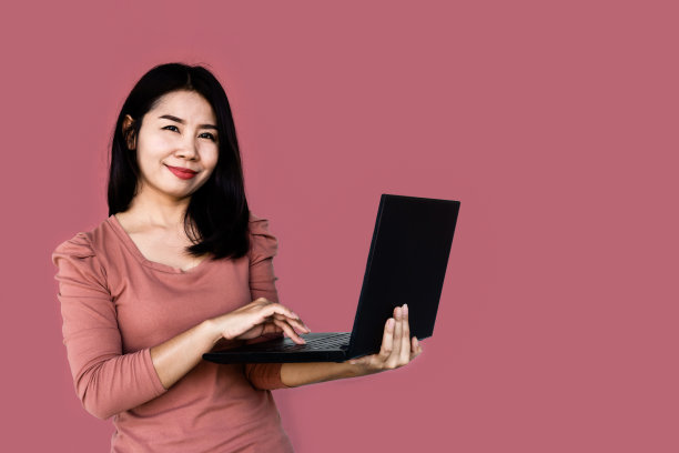 美丽的亚洲女人拿着笔记本电脑站在粉红色背景前，学习和网上购物图片下载