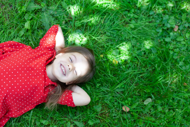 一个可爱的小女孩躺在草地上微笑的照片图片下载
