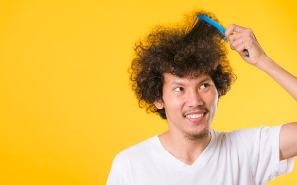 亚洲男子梳理卷曲的头发在黄色的背景图片下载