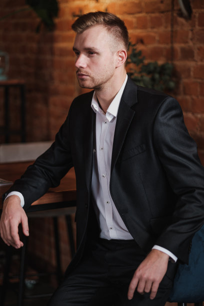 在具有阁楼内饰的餐厅里，一位穿着西装和衬衫的英俊的年轻金发络腮胡男子。他坐在桌旁，读一本杂志。图片下载