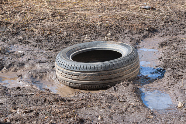 一个破旧的汽车轮胎在泥和水坑里打滚。环境污染。生态问题。图片下载