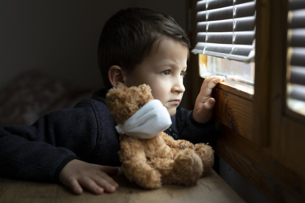 冠状病毒隔离期间，悲伤的小男孩透过窗户看外面。图片下载