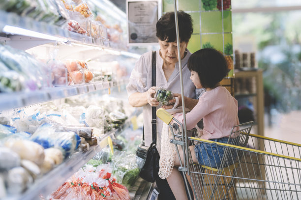 周末，中国祖母和孙女在超市冷藏区购买蔬菜，孙女坐在购物车里图片下载