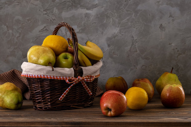 静物，新鲜多汁的水果装在一个篮子里，放在一张旧墙背景的木桌上图片下载