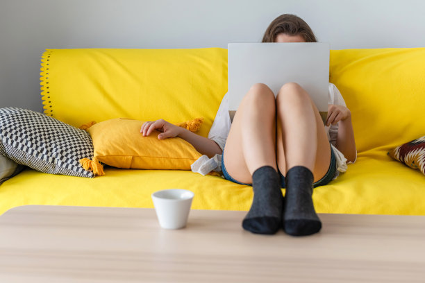 女自由职业者坐在沙发上，把笔记本电脑放在袜子里，把腿放在桌子上。在家里工作。的概念。杯咖啡。放松在家里。图片下载