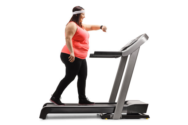 超重女性在跑步机上锻炼，看着手臂智能手环图片下载