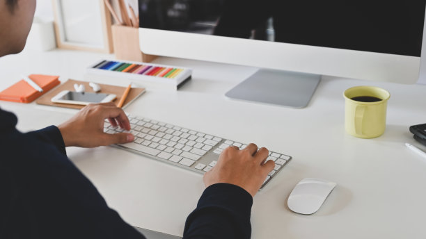 裁剪的镜头，聪明的人打字键盘在黑屏电脑显示器和坐在现代工作桌子与舒适的工作环境为背景。图片下载