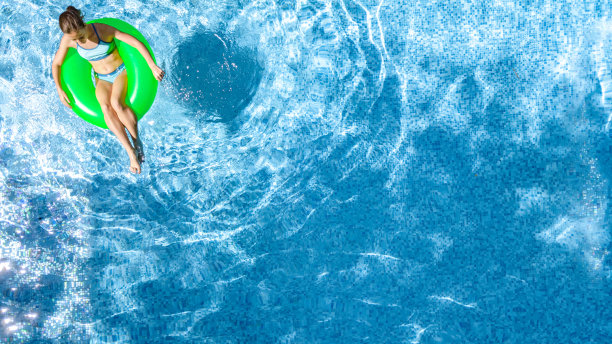 活跃的年轻女孩在游泳池空中俯瞰从上面，孩子放松和游泳在充气圈甜甜圈和在水上有乐趣的家庭度假，热带度假胜地图片下载