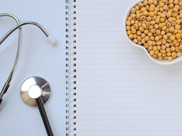 心形碗里的大豆和听诊器在笔记本上，健康食品的概念。植物蛋白质。顶部视图与复制空间。图片下载