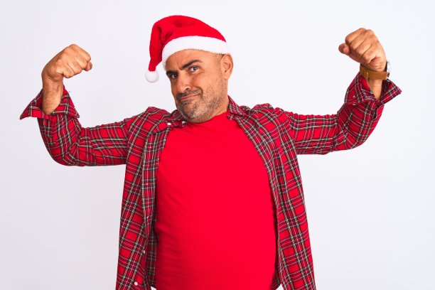 中年男人戴着圣诞老人帽子，展示手臂肌肉，面带骄傲的笑容。健身概念图片下载