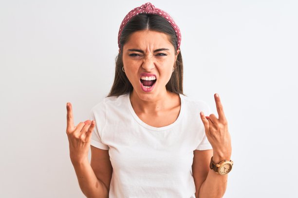 年轻美丽的女人穿着休闲t恤和冠冕在孤立的白色背景大喊与疯狂的表情做摇滚符号与手举起。音乐明星。沉重的概念。图片下载