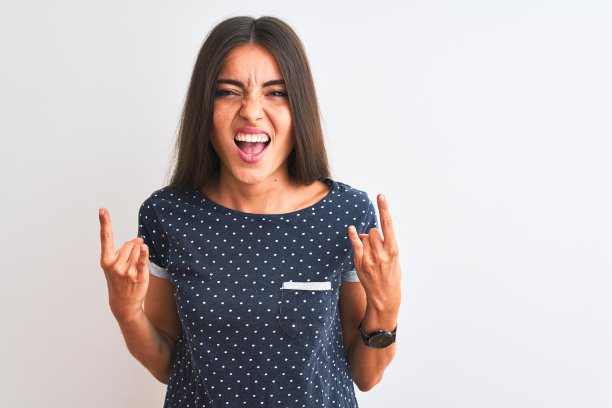 年轻美丽的女人穿着蓝色休闲t恤站在孤立的白色背景大喊与疯狂的表情做摇滚符号与手举起。音乐明星。沉重的概念。图片下载